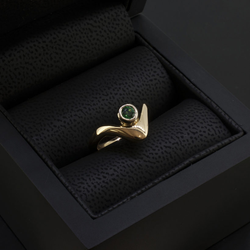 Ladies Solitaire Emerald Ring, Rub over Set Design in 18kt White and Yellow Gold, Round Emerald 0.10ct in an 18kt Rub over, Wave Design Detail