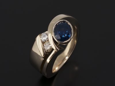 Oval Cut Sapphire, 1.61ct Rub over Set in 18kt Yellow Gold with Tension Set Round Brilliant Cut Diamonds. 0.23ct (2) in a Twist Design