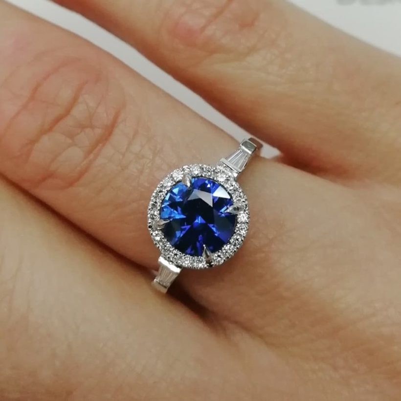 Round Brilliant Cut Sapphire 1.49ct with Tapered Baguette Cut Diamonds 0.20ct Total and Round Brilliant Cut Diamonds in a Platinum Halo Design Ladies Ring