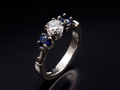 Platinum Trilogy Ring with Round Brilliant Diamond 0.46ct F Colour VS Clarity Minimum and 2 x Round Sapphires 0.57ct total. Letters ‘J’ and ‘R’ located on each shoulder