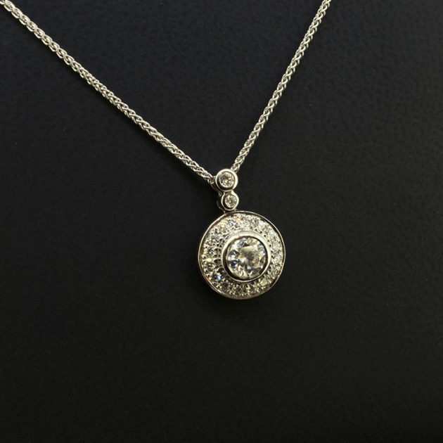 Round Brilliant Cut Centre Diamond 0.50ct with Round Brilliant Cut Diamonds in Halo and Bale 0.29ct Total in a 18kt White Gold Rub Over and Halo Pavé Set Pendant Design with Spiga Chain.