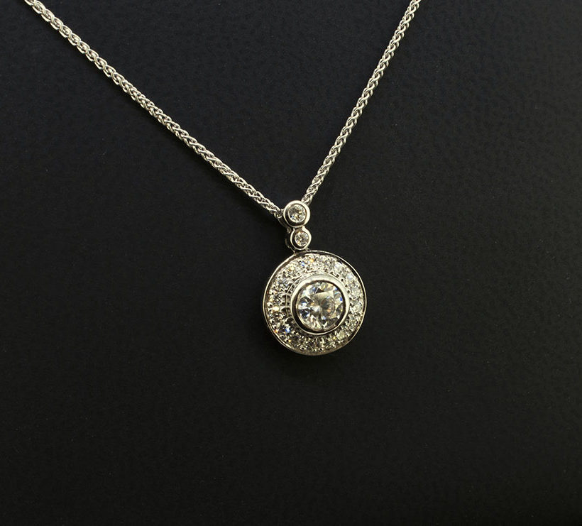 Round Brilliant Cut Centre Diamond 0.50ct with Round Brilliant Cut Diamonds in Halo and Bale 0.29ct Total in a 18kt White Gold Rub Over and Halo Pavé Set Pendant Design with Spiga Chain.