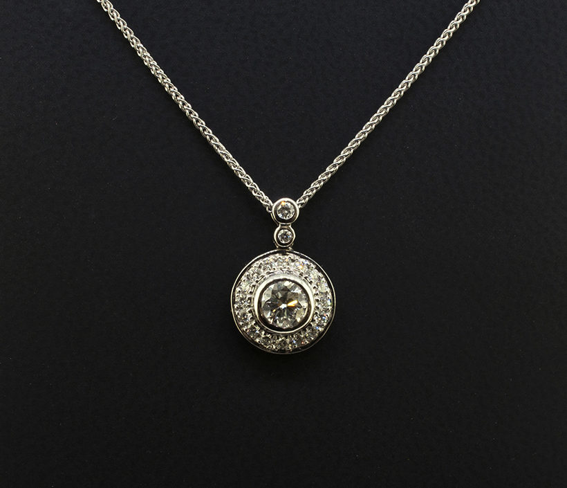 Round Brilliant Cut Centre Diamond 0.50ct with Round Brilliant Cut Diamonds in Halo and Bale 0.29ct Total in a 18kt White Gold Rub Over and Halo Pavé Set Pendant Design with Spiga Chain.