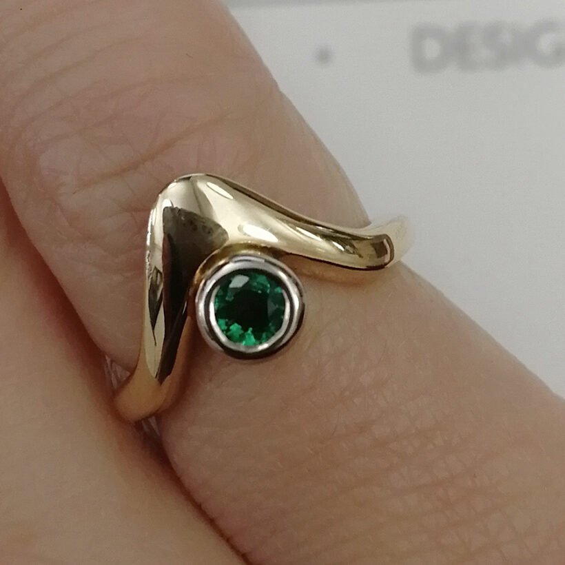 Ladies Solitaire Emerald Ring, Rub over Set Design in 18kt White and Yellow Gold, Round Emerald 0.10ct in an 18kt Rub over, Wave Design Detail