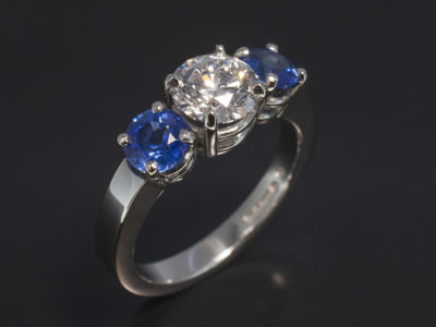 Bespoke coloured stone ring, platinum claw set trilogy with round brilliant cut diamond and 2 round blue sapphires