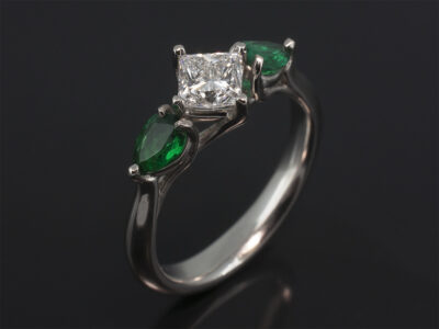 Platinum Claw Set Trilogy Design. Princess Cut Diamond, 0.62ct, E Colour, VS1 Clarity. Pear Shape Emeralds, 0.44ct (2)