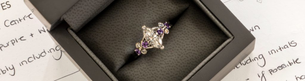 A multi stone bespoke engagement ring by Blair and Sheridan featuring a Marquise diamond centre stone and a mix of diamond and purple sapphire round cut side stones